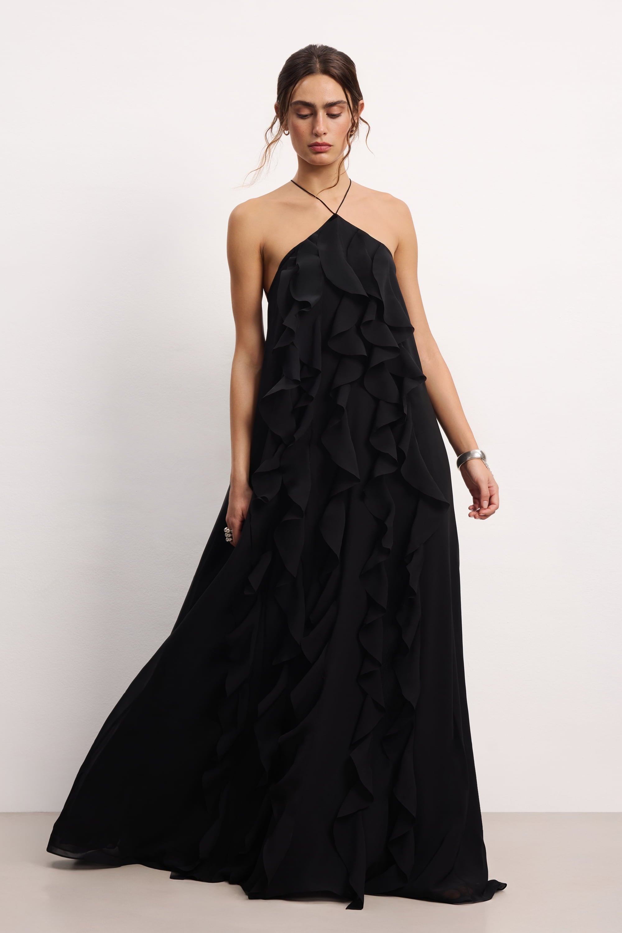 Woman wearing a black halter neck Illusion dress with thin straps and ruffled layers on a white background, front view